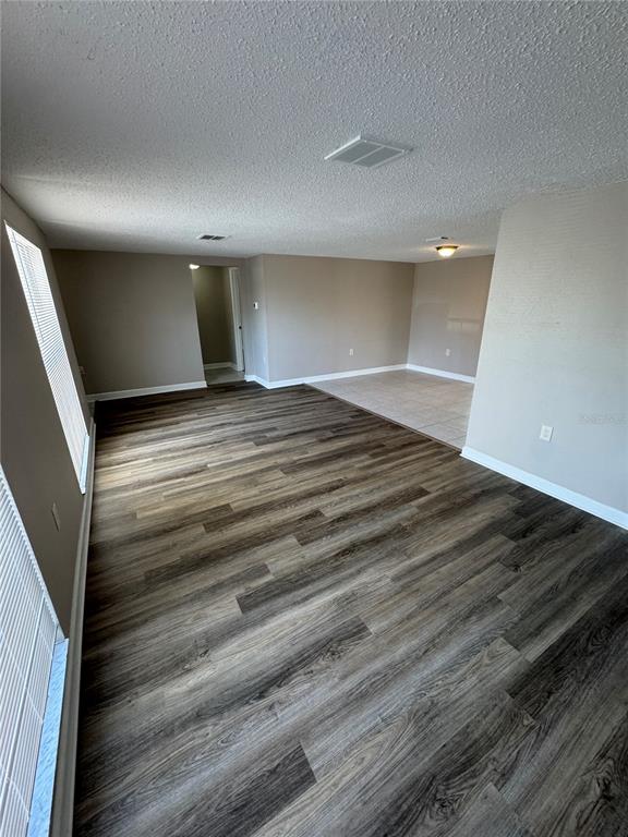 An empty room with wood-look flooring, beige walls, and an adjacent tiled area — 6135 SEABREEZE DRIVE, PORT RICHEY, FL