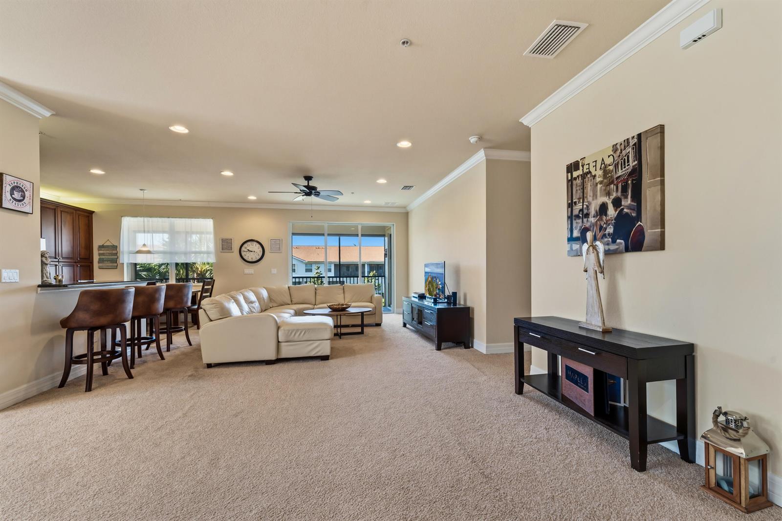 An open-concept living room features a beige sectional sofa, a kitchen island, and carpeted floors — 6513 Monterey Point # 201, Naples FL 34105, NAPLES, FL