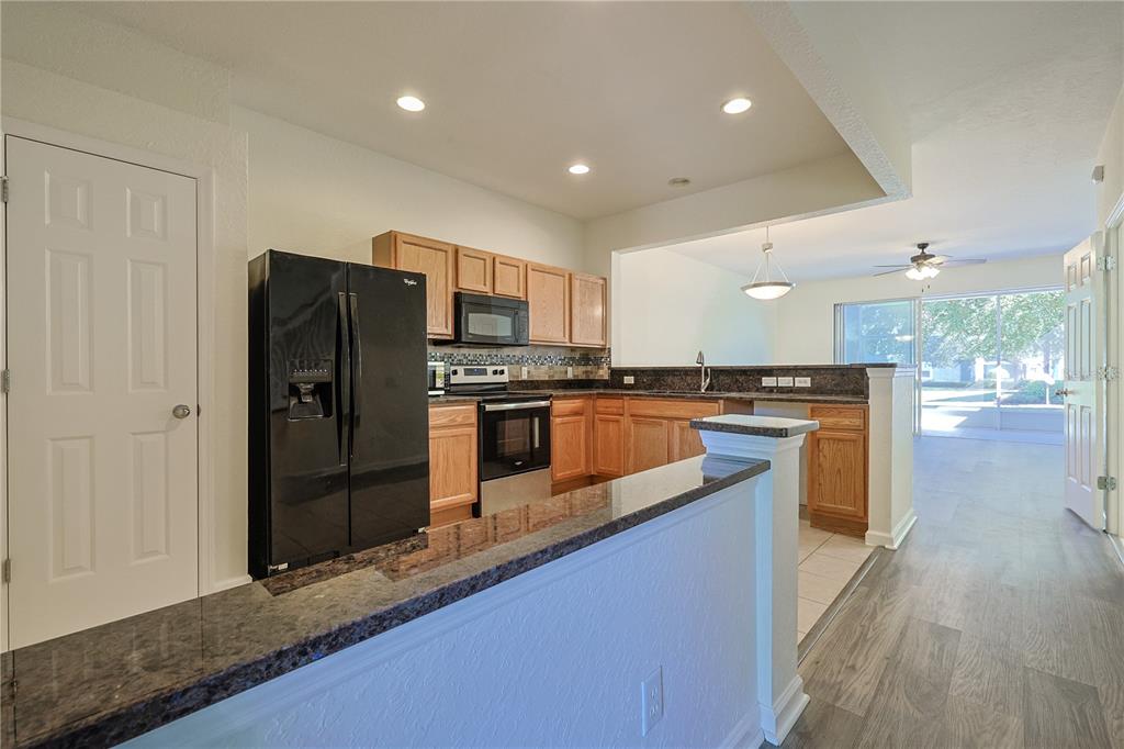 A kitchen with oak cabinets, black appliances, and granite countertops overlooks an open living area — 4116 SW 54TH CIRCLE, OCALA, FL
