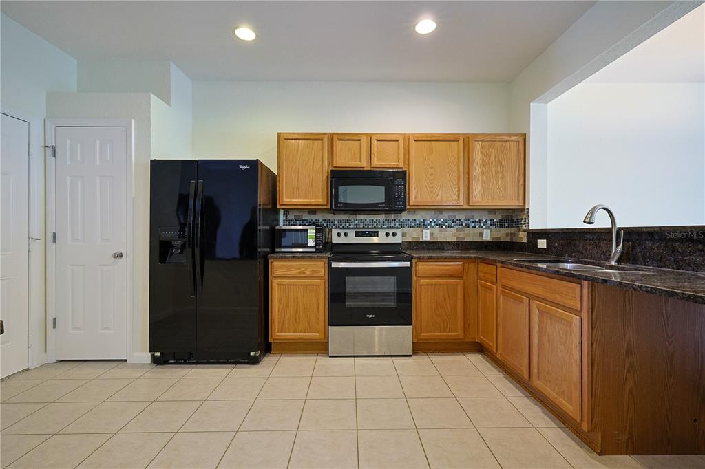 A kitchen features light wood cabinets, dark granite countertops, and black appliances on tiled floors — 4116 SW 54TH CIRCLE, OCALA, FL