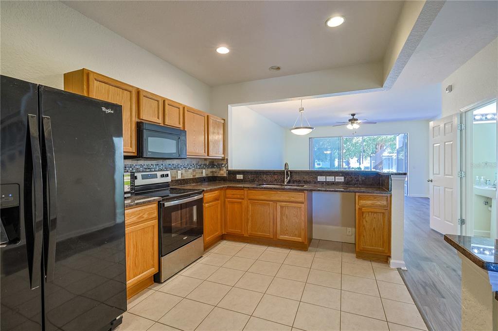 A kitchen with wood cabinets, dark countertops, tile flooring, and a black refrigerator and stove — 4116 SW 54TH CIRCLE, OCALA, FL