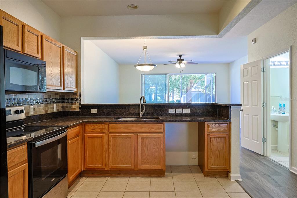 A kitchen with wood cabinets, dark countertops, a tile backsplash, and an open pass-through window — 4116 SW 54TH CIRCLE, OCALA, FL