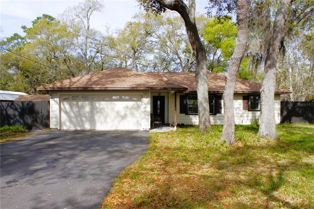 A single-story house with a tan exterior, a two-car garage, and mature trees in front — 3201 BARTLETT STREET, SPRING HILL, FL