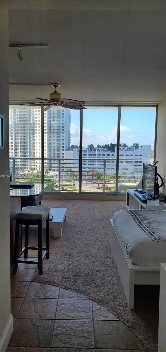 A bedroom with a ceiling fan, carpeted floor, and large windows overlooking a city skyline — 1720 Harrison St # 10G, Hollywood FL 33020, HOLLYWOOD, FL