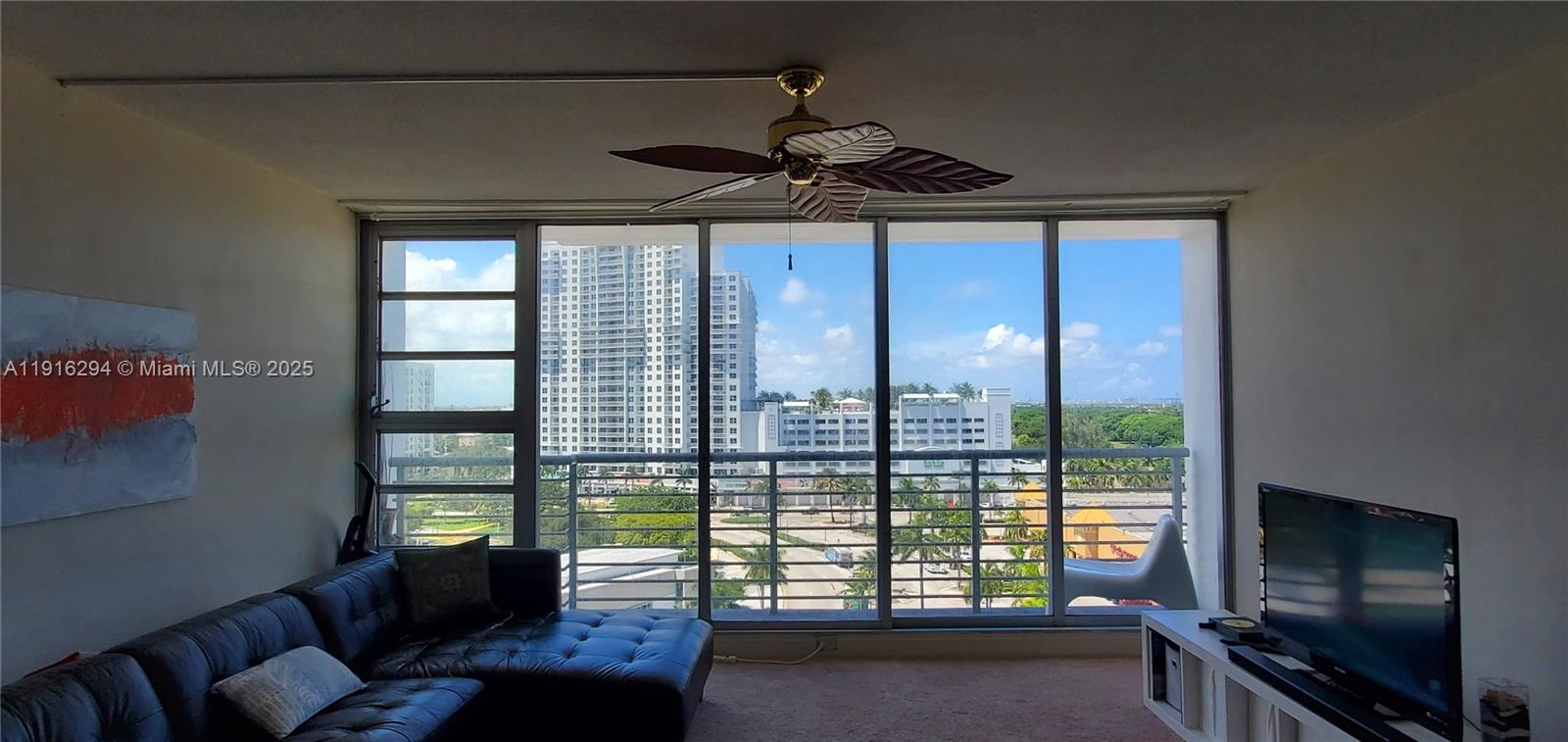 A living room features a dark leather sectional, a television, and floor-to-ceiling windows overlooking buildings — 1720 Harrison St # 10G, Hollywood FL 33020, HOLLYWOOD, FL