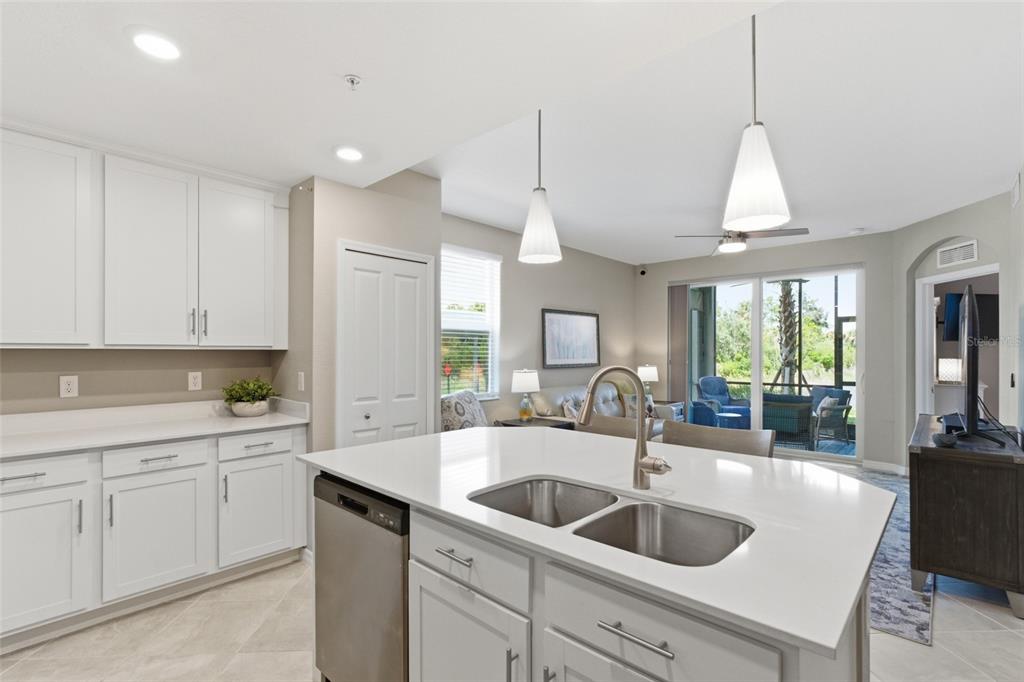 A kitchen island with a double sink faces a living area with a sliding glass door — 14151 HERITAGE LANDING BOULEVARD UNIT 1011, PUNTA GORDA, FL