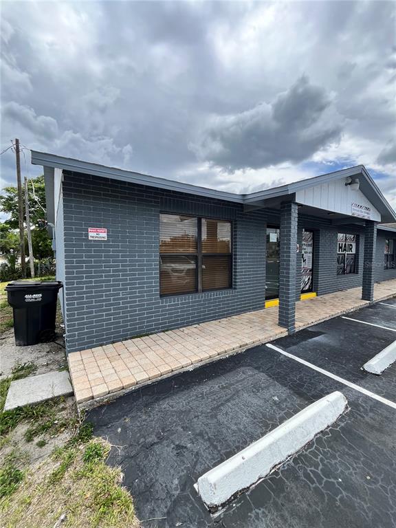 A gray brick commercial building features a paved walkway and a black trash bin outside — 7218 CONGRESS ST., NEW PORT RICHEY, FL