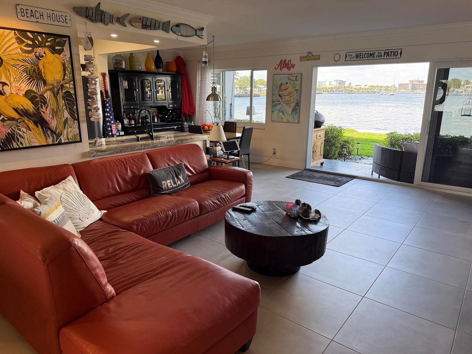 A living room with a red sectional sofa, round wooden coffee table, and waterfront patio view — 1201 S Riverside Drive # 106, Pompano Beach FL 33062, POMPANO BEACH, FL