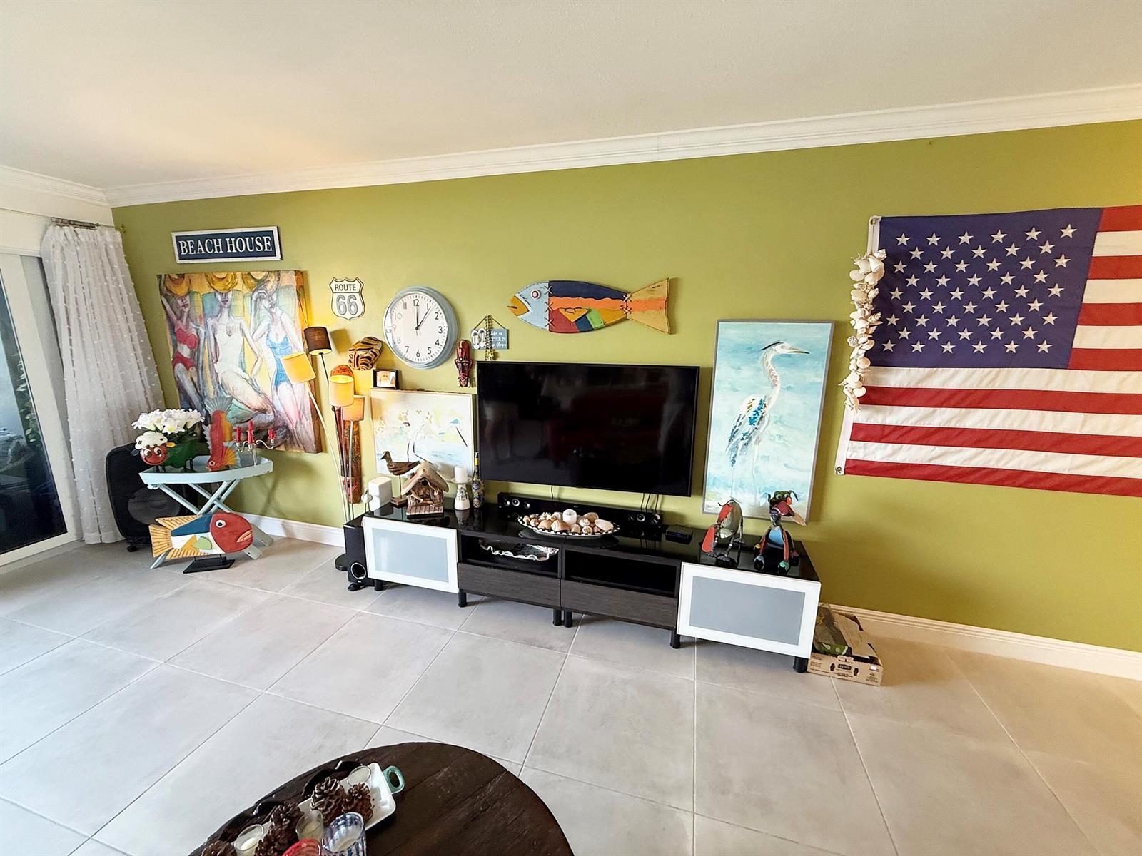 A living room features a green wall decorated with art, a television, and an American flag — 1201 S Riverside Drive # 106, Pompano Beach FL 33062, POMPANO BEACH, FL