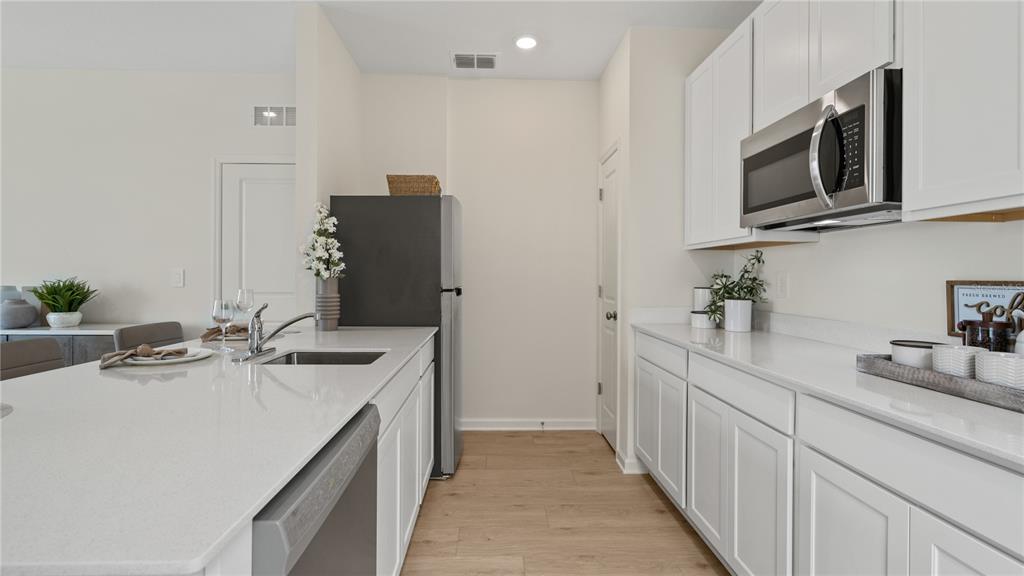 A modern kitchen features white cabinets, a quartz island with a sink, and stainless appliances — 2214 JENNIO DRIVE, HAINES CITY, FL
