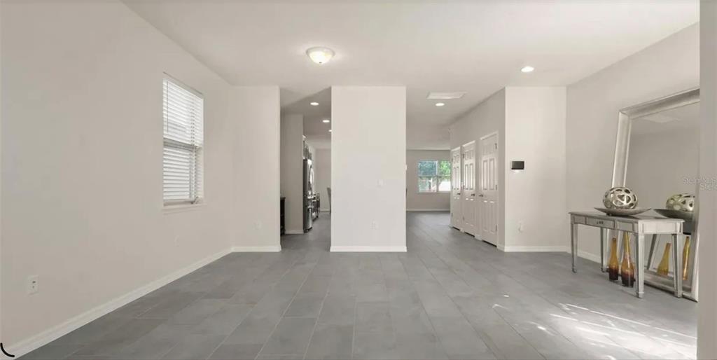 A bright, open-concept room features gray tile flooring, white walls, and a central partition wall — 17243 GOLDCREST LOOP, CLERMONT, FL