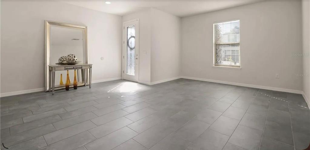 A bright room with gray tile flooring, a glass-paneled front door, and a large mirror — 17243 GOLDCREST LOOP, CLERMONT, FL