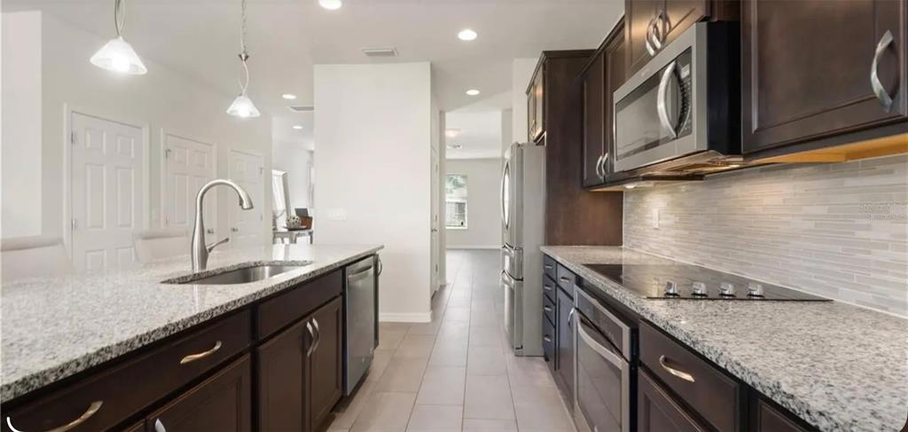A kitchen with dark wood cabinets, granite countertops, stainless steel appliances, and tile flooring — 17243 GOLDCREST LOOP, CLERMONT, FL