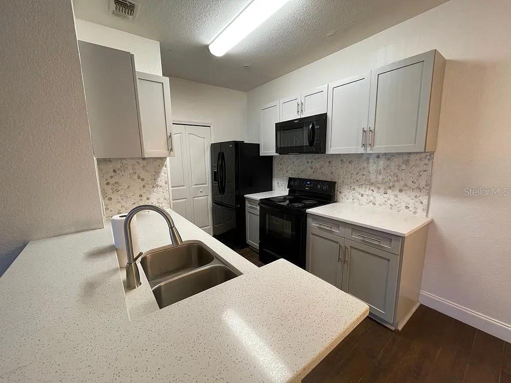 A kitchen features gray cabinets, white countertops, a double sink, and black appliances — 5821 LEGACY CRESCENT PLACE UNIT 102, RIVERVIEW, FL
