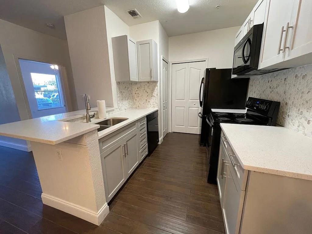 A kitchen features light gray cabinets, white countertops, a tile backsplash, and dark wood flooring — 5821 LEGACY CRESCENT PLACE UNIT 102, RIVERVIEW, FL