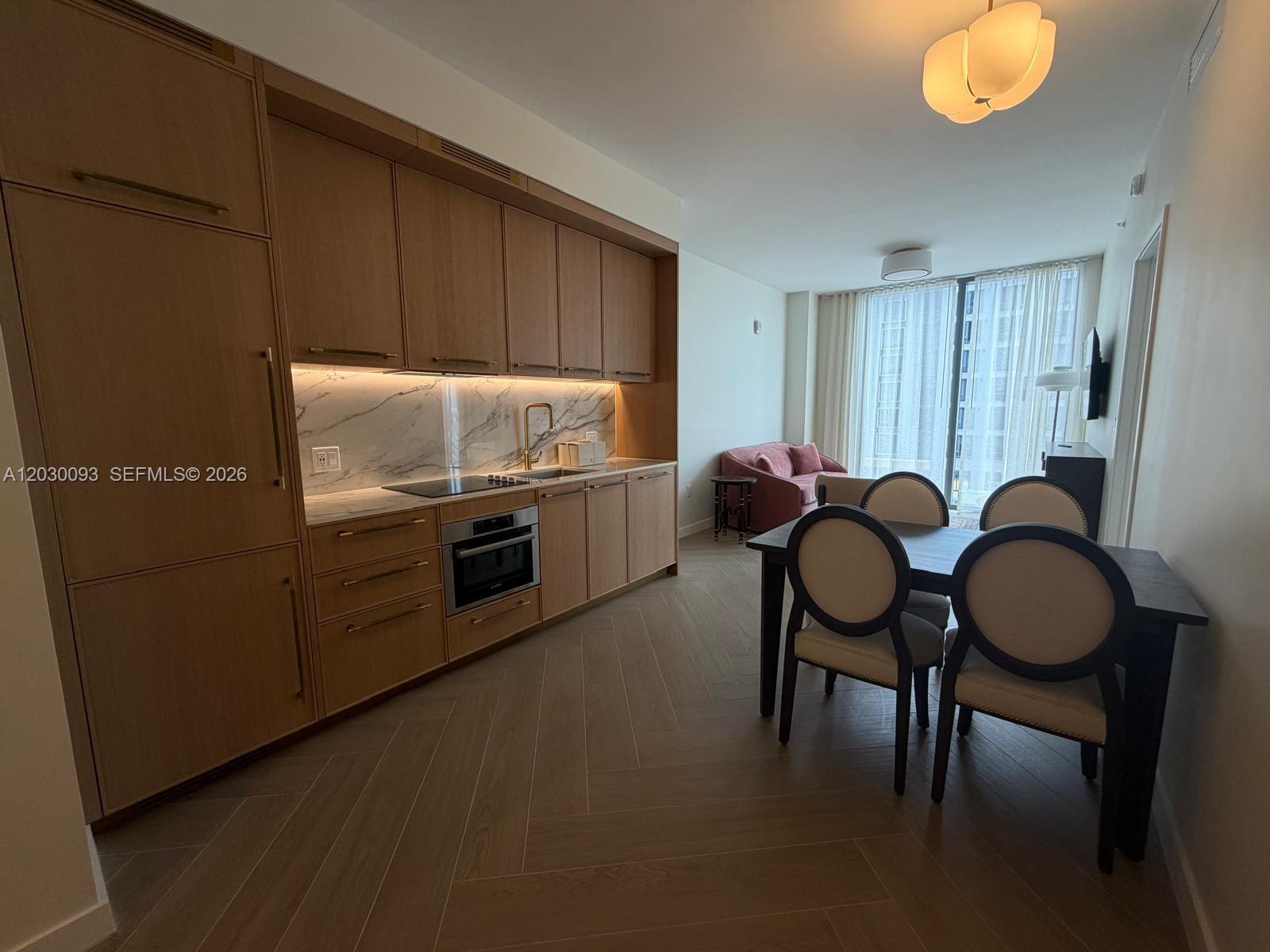 A modern kitchen with wood cabinetry and marble backsplash opens into a dining and living area — 2700 NW 2ND AVE # 342, Miami FL 33127, MIAMI, FL