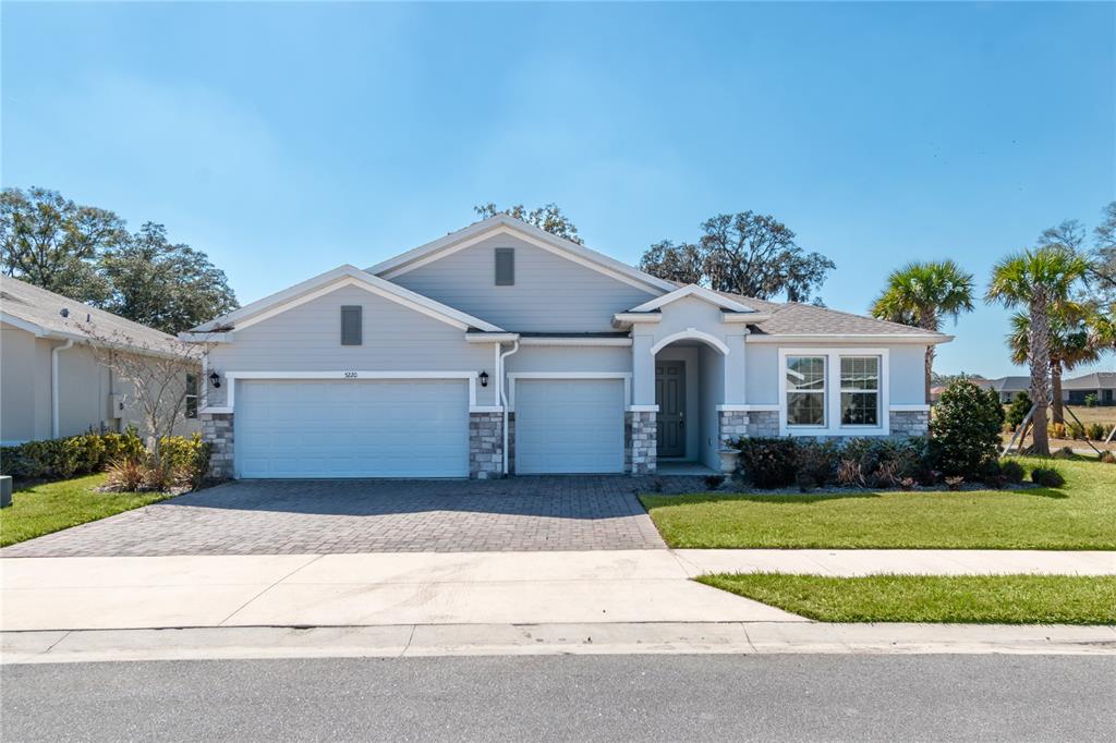 A single-story house with a light blue exterior, stone accents, and a three-car garage — 5220 NW 46TH LANE ROAD, OCALA, FL