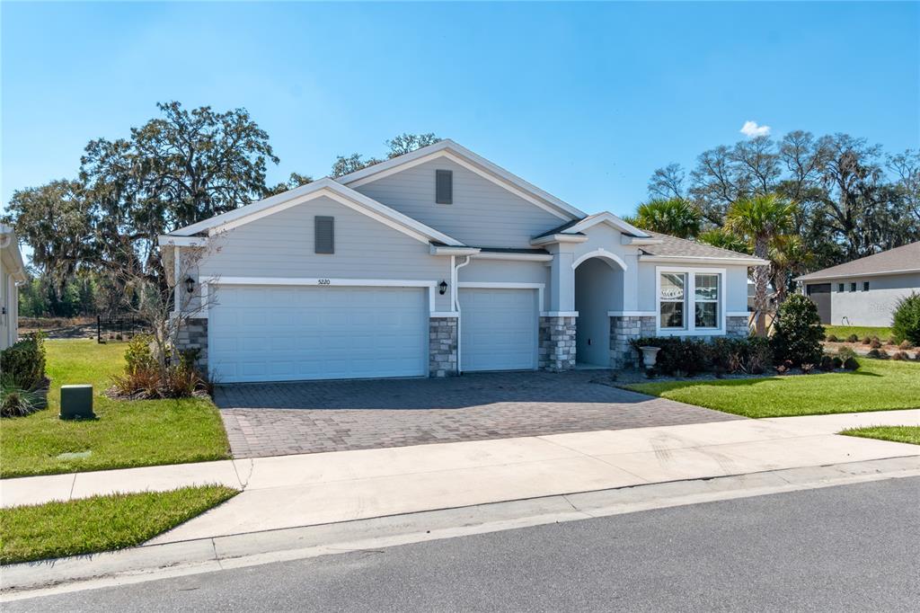 A single-story house with a gray exterior, stone accents, and a three-car garage — 5220 NW 46TH LANE ROAD, OCALA, FL