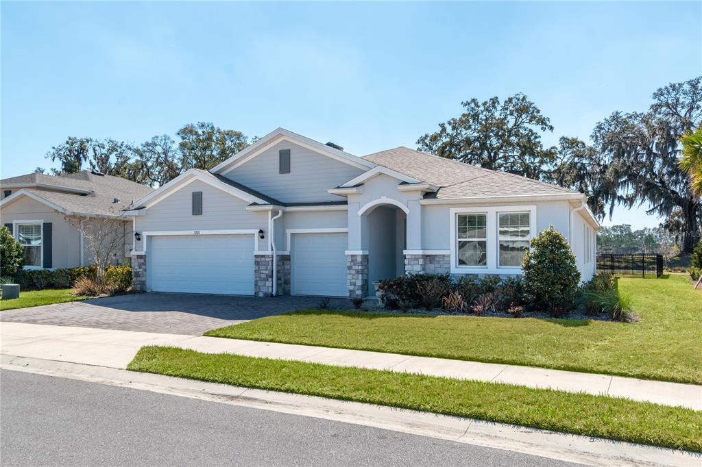 A single-story suburban house with a three-car garage, stone accents, and a paved driveway — 5220 NW 46TH LANE ROAD, OCALA, FL