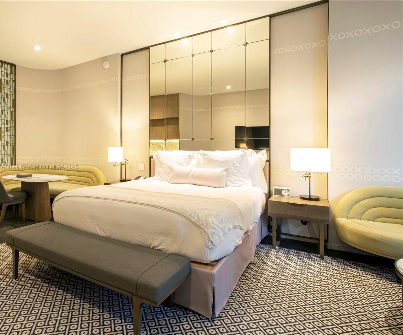 A bedroom features a bed with a mirrored headboard, patterned carpet, and two bedside lamps — 801 S Miami Ave # 611, Miami FL 33130, MIAMI, FL