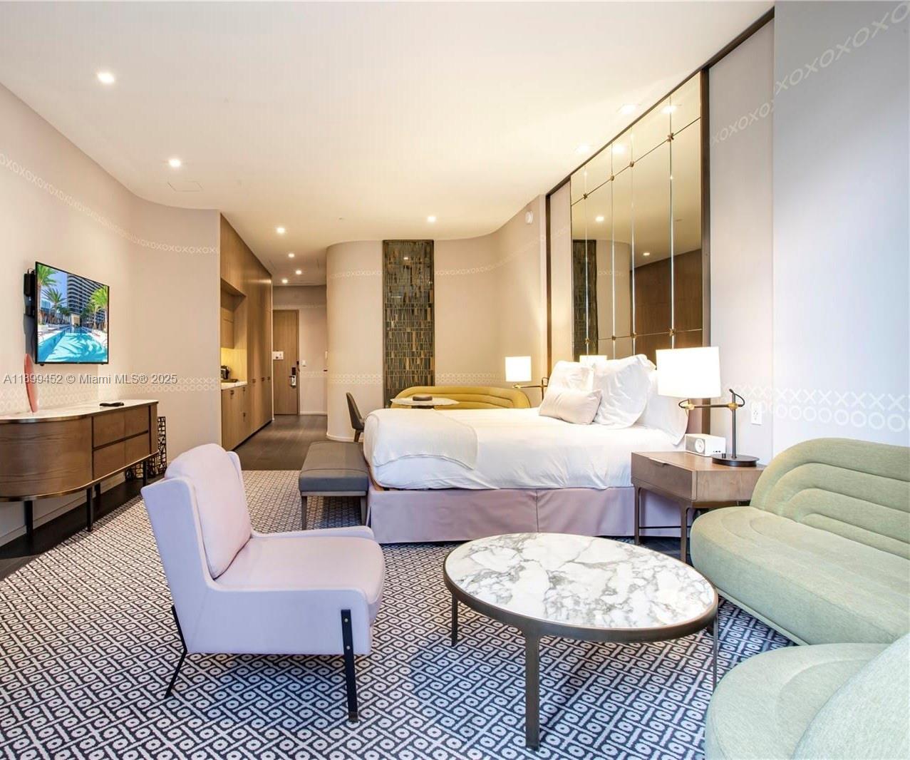 A modern hotel bedroom features a king bed, patterned carpet, seating area, and mirrored wall — 801 S Miami Ave # 611, Miami FL 33130, MIAMI, FL