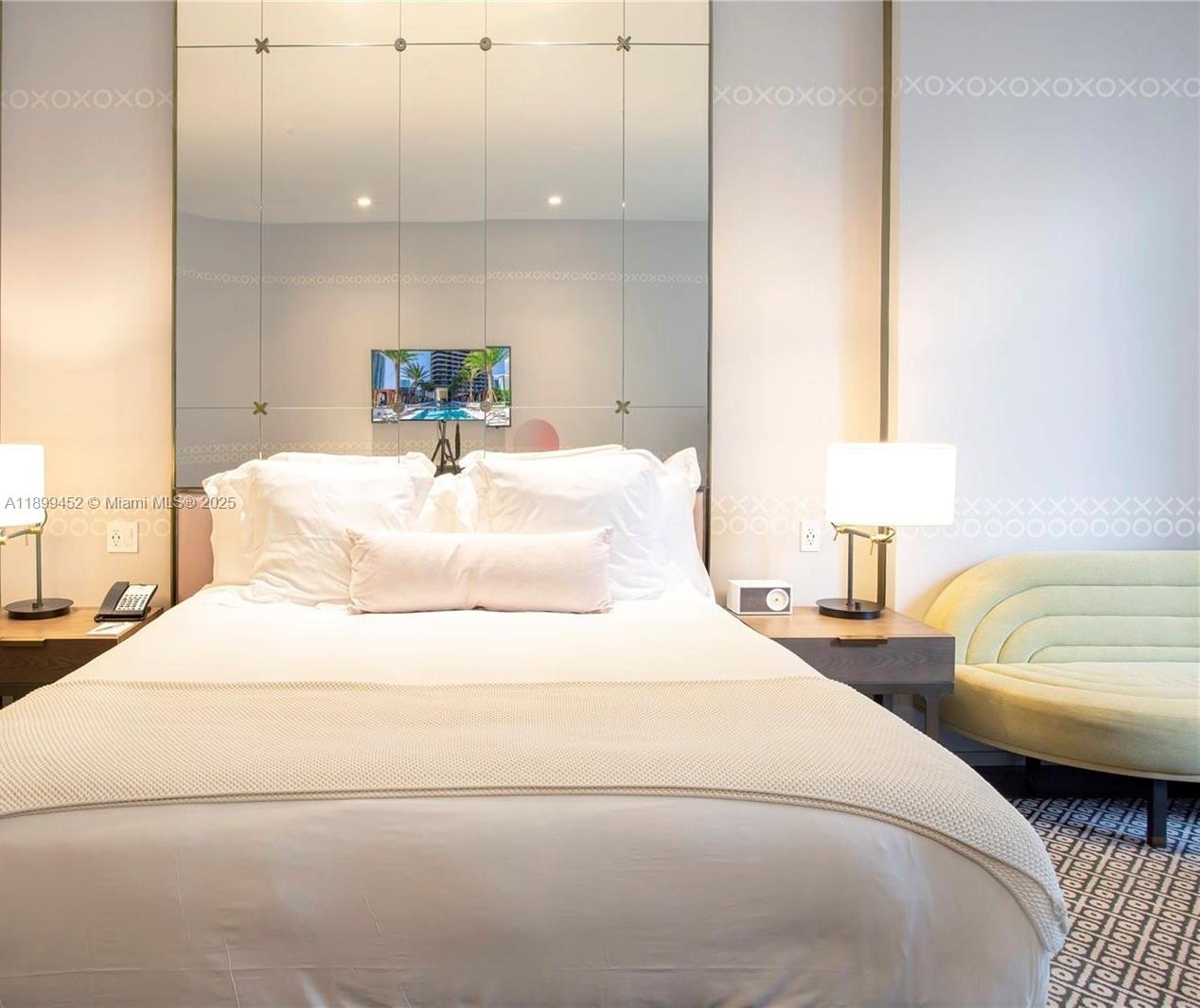 A bedroom features a bed with white linens, a large mirrored headboard, and a curved sofa — 801 S Miami Ave # 611, Miami FL 33130, MIAMI, FL