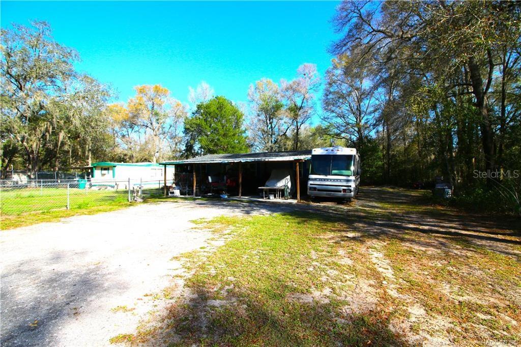 A large covered carport shelters a motorhome on a gravel lot near a mobile home — 4629 E BOW N ARROW LOOP, INVERNESS, FL