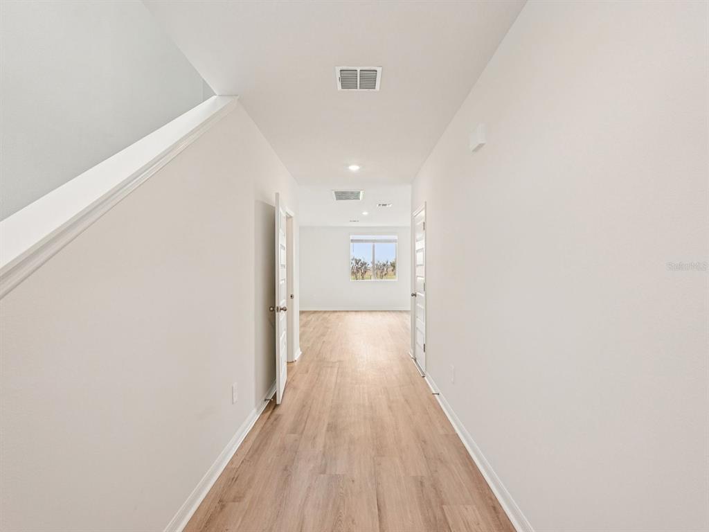 A hallway with light wood-look flooring leads to a room with a window — 9130 DALERA COVE, PALMETTO, FL