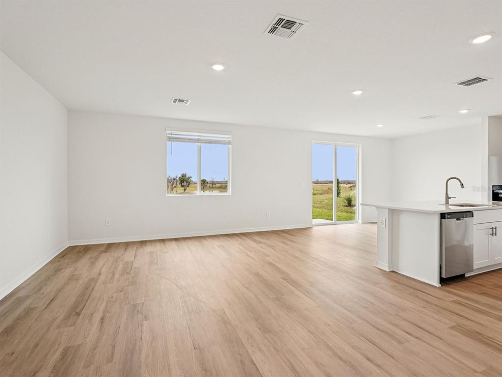An open-concept living area features light wood-look flooring, white walls, recessed lighting, and a kitchen — 9130 DALERA COVE, PALMETTO, FL