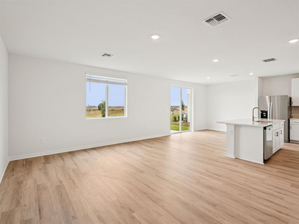 An open-concept kitchen and living area features white cabinetry, a kitchen island, and wood-look flooring — 9130 DALERA COVE, PALMETTO, FL