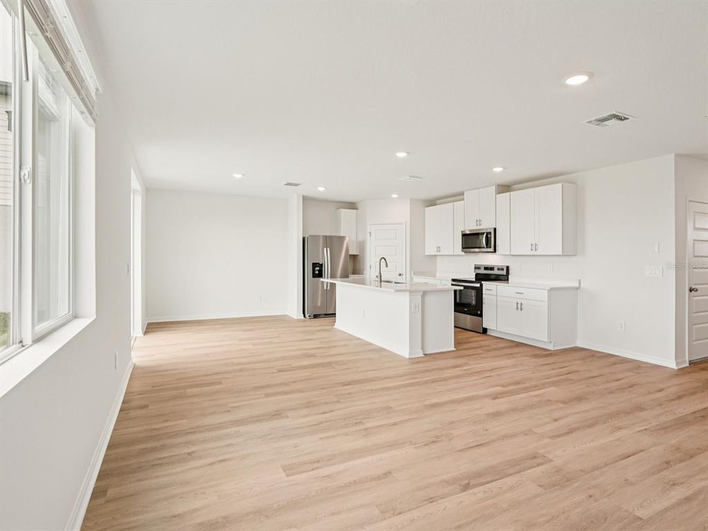 A bright, open-concept kitchen features white cabinetry, stainless steel appliances, and light wood-look flooring — 9130 DALERA COVE, PALMETTO, FL