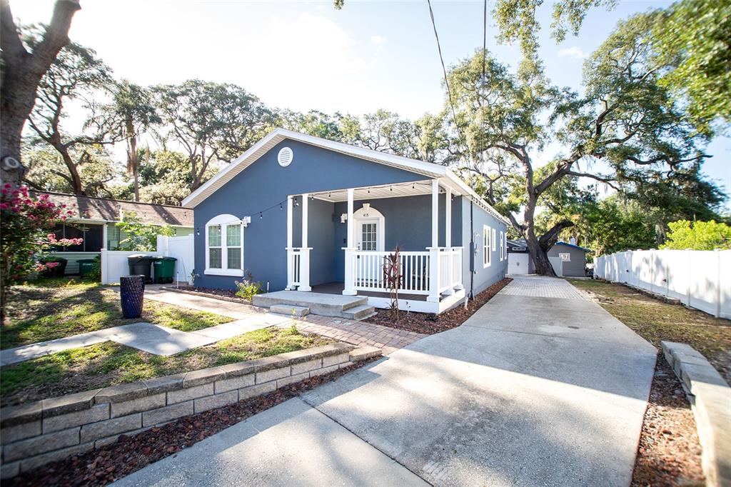 A blue single-story house features a white front porch, a concrete driveway, and mature trees — 415 DR ML KING JR STREET N, SAFETY HARBOR, FL