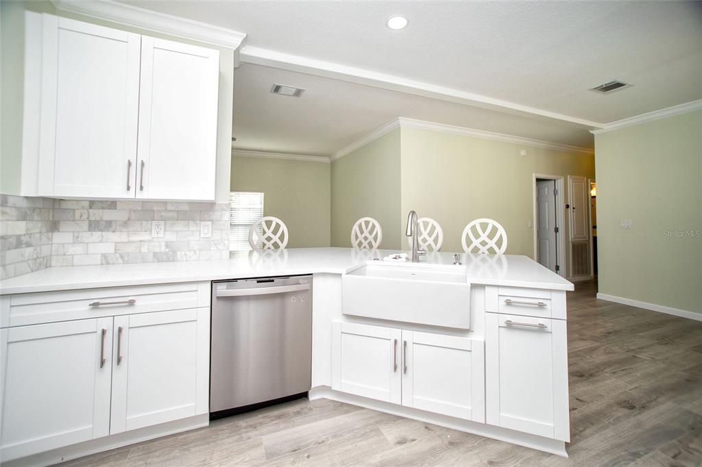 A kitchen features white cabinets, a farmhouse sink, stainless steel dishwasher, and light wood flooring — 415 DR ML KING JR STREET N, SAFETY HARBOR, FL
