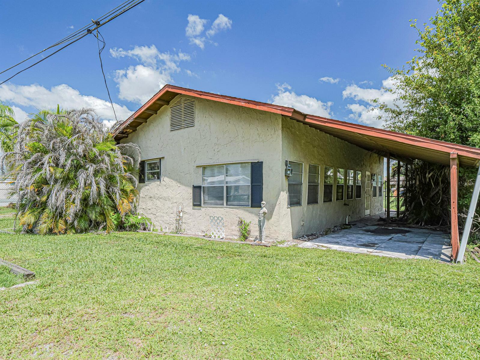 A single-story house with a stucco exterior, a metal carport, and a large palm tree — 1040 Lissie Lane, Okeechobee FL 34974, OKEECHOBEE, FL