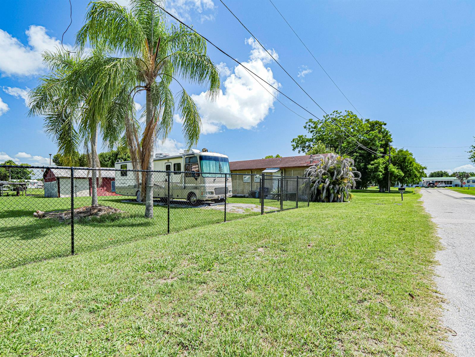 A chain-link fence surrounds a grassy yard containing a motorhome and a small building — 1040 Lissie Lane, Okeechobee FL 34974, OKEECHOBEE, FL