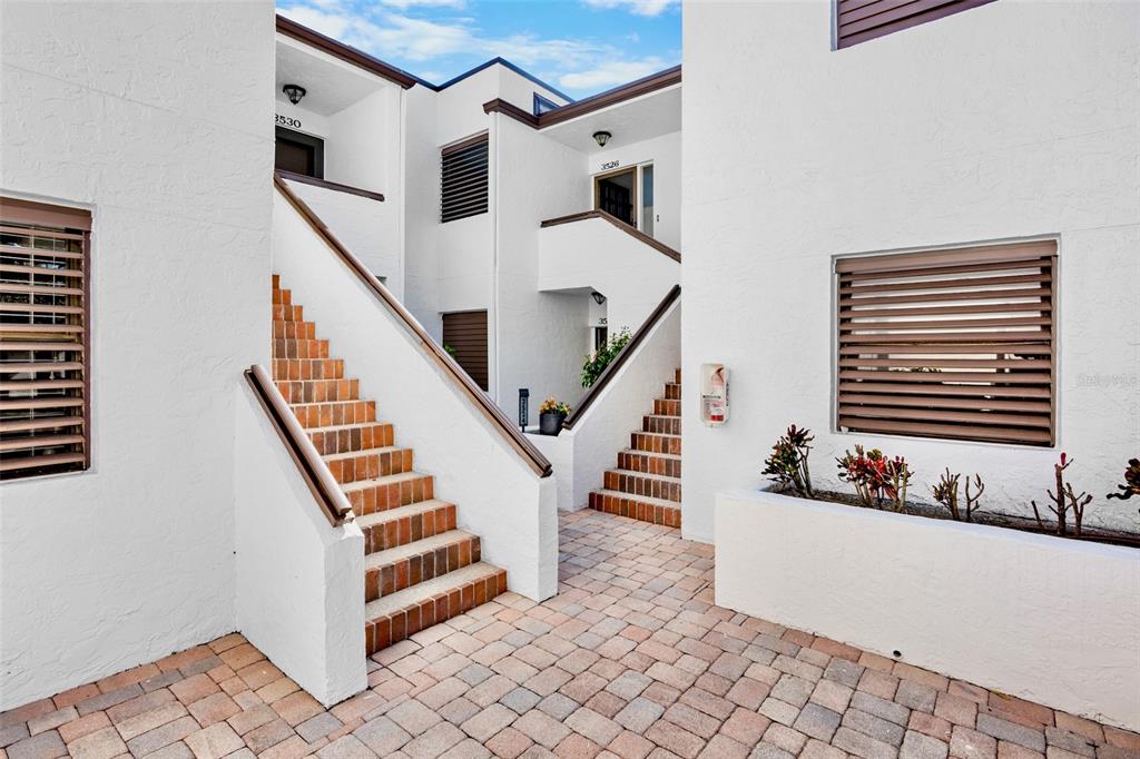 Exterior view of a white stucco apartment building with brick stairs and a paved courtyard — 3526 RICHWOOD LINK UNIT 48, SARASOTA, FL