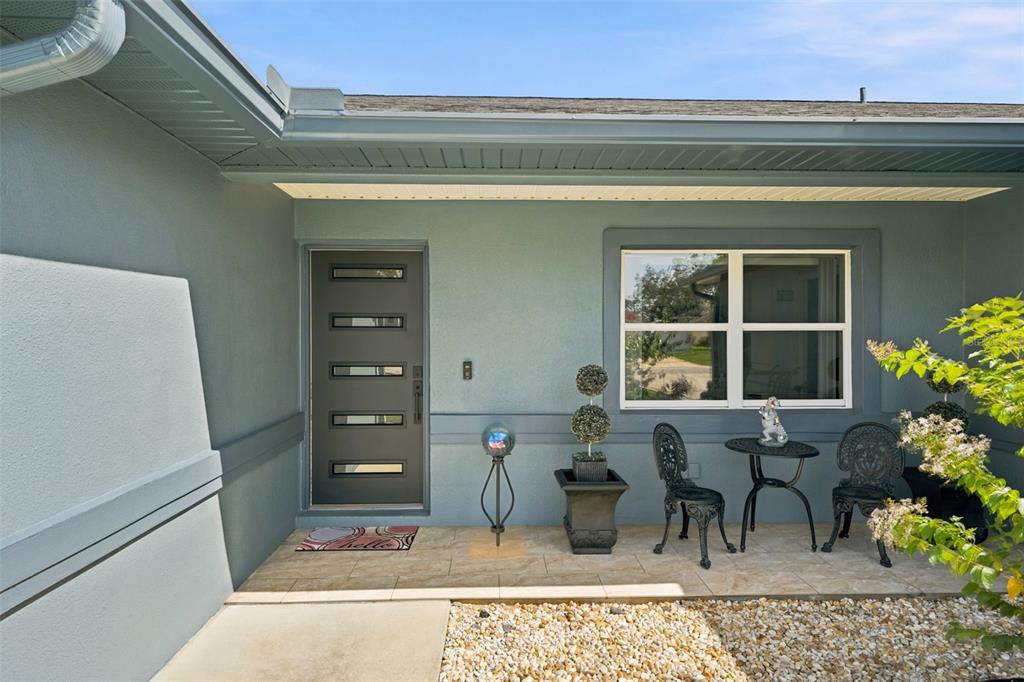 The exterior view shows a front entryway with a gray door, window, and patio furniture — 13323 STEVES COURT, SPRING HILL, FL