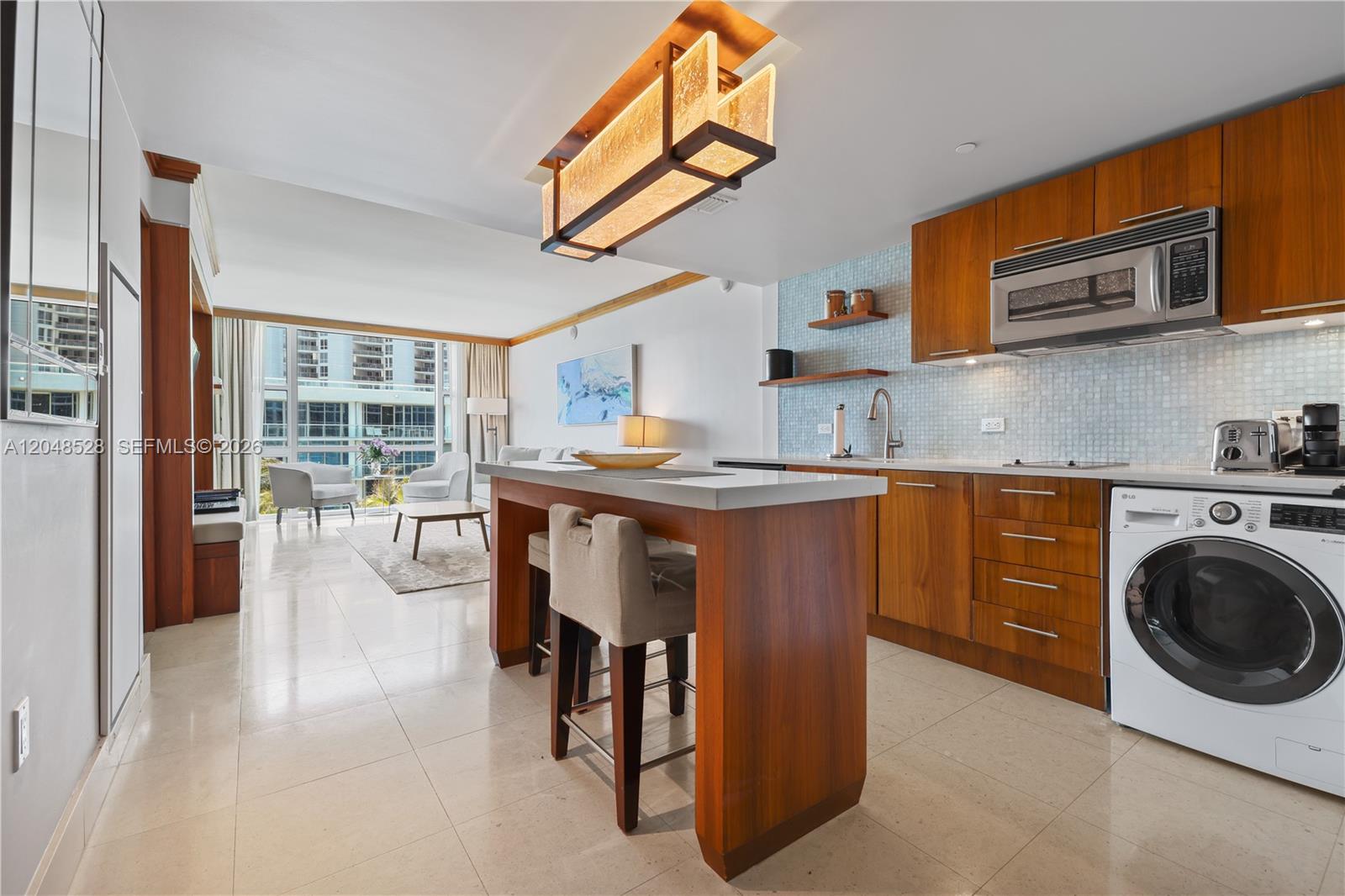 A modern kitchen with wood cabinets and a breakfast bar opens into a living area — 6801 Collins Ave # 516, Miami Beach FL 33141, MIAMI BEACH, FL