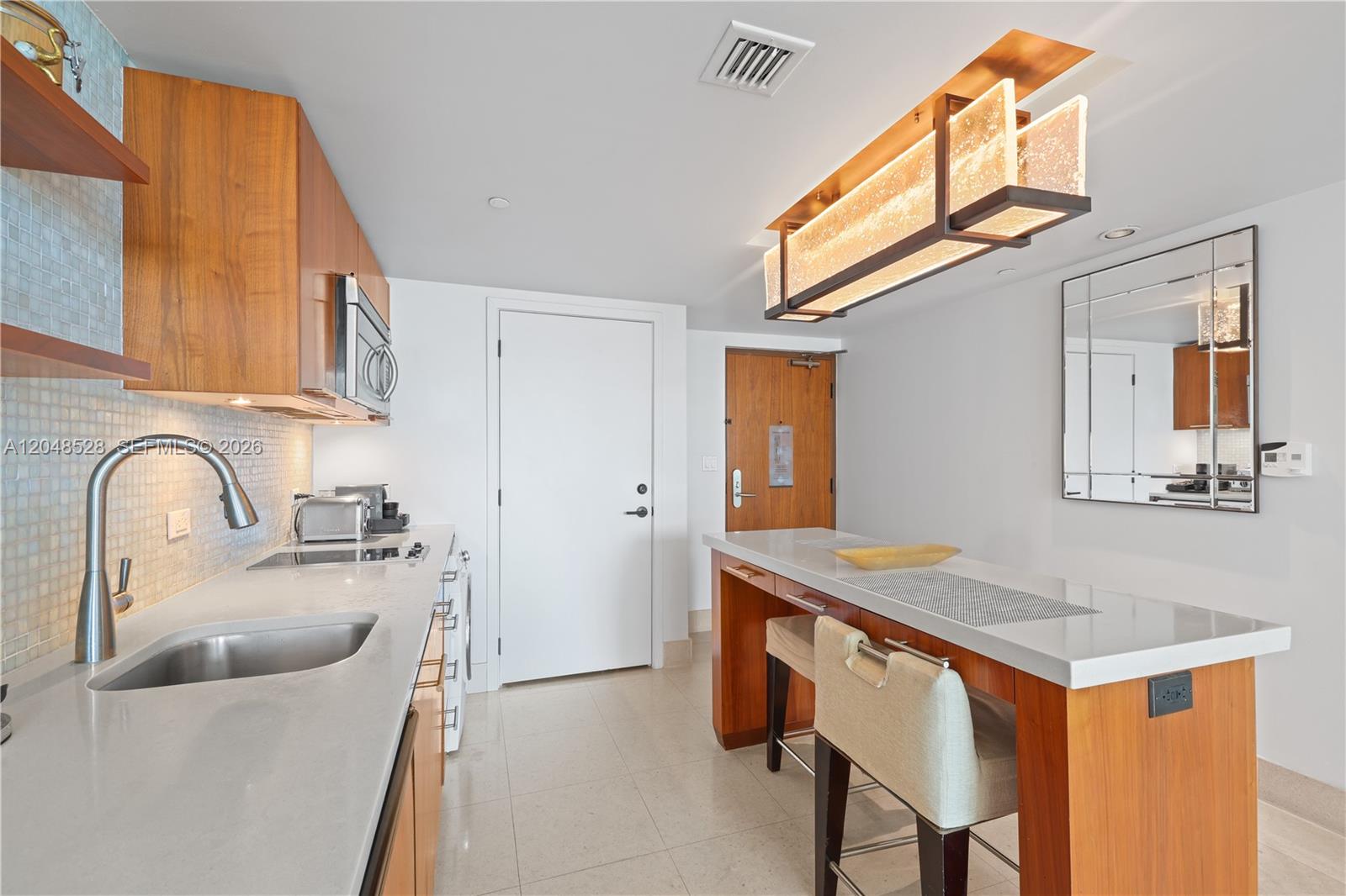 A modern kitchen features wood cabinetry, a stone countertop, and a breakfast bar with stools — 6801 Collins Ave # 516, Miami Beach FL 33141, MIAMI BEACH, FL