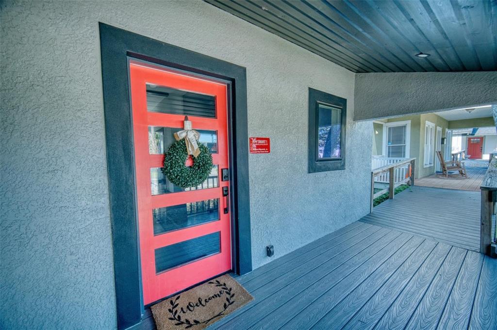 A bright orange front door with a wreath sits on a covered wooden porch — 141 AVENUE E SW, WINTER HAVEN, FL