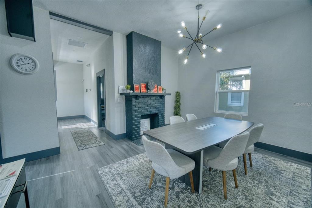 A dining room features a dark brick fireplace, a modern chandelier, and light wood flooring — 141 AVENUE E SW, WINTER HAVEN, FL