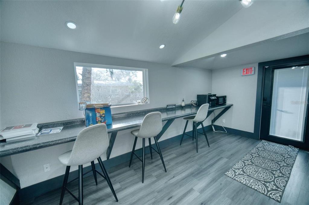 A home office features a long built-in desk, two bar stools, and grey flooring — 141 AVENUE E SW, WINTER HAVEN, FL