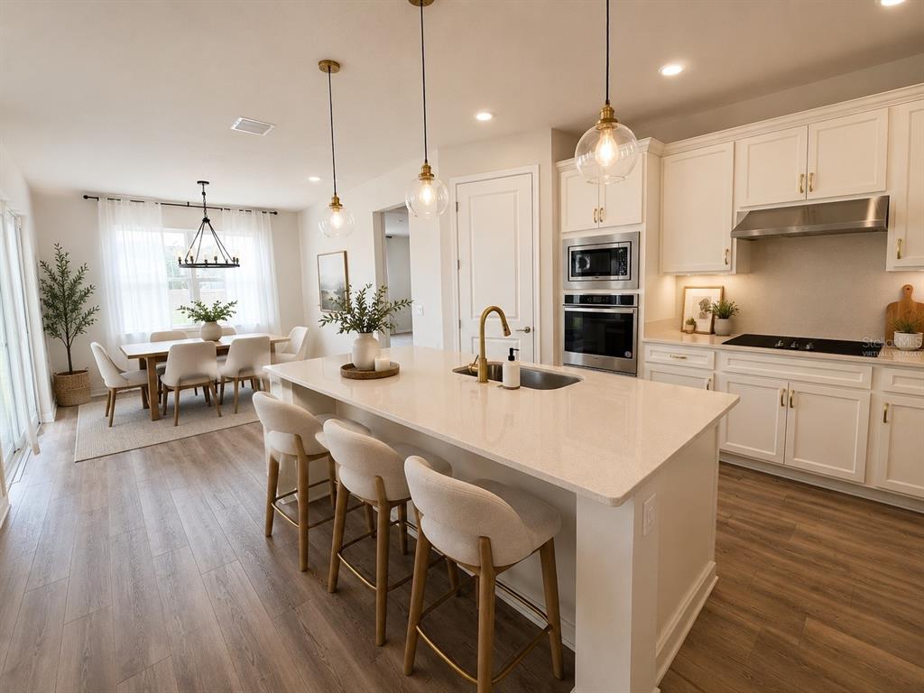 A modern kitchen features a large quartz island, white cabinetry, and an adjacent dining area — 2602 AUTUMN PEACE DRIVE, KISSIMMEE, FL