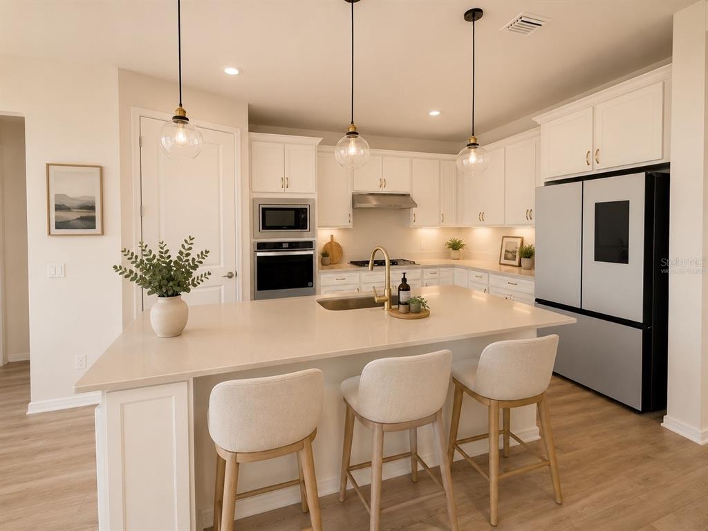 A modern kitchen features white cabinetry, a large quartz island with seating, and stainless appliances — 2602 AUTUMN PEACE DRIVE, KISSIMMEE, FL