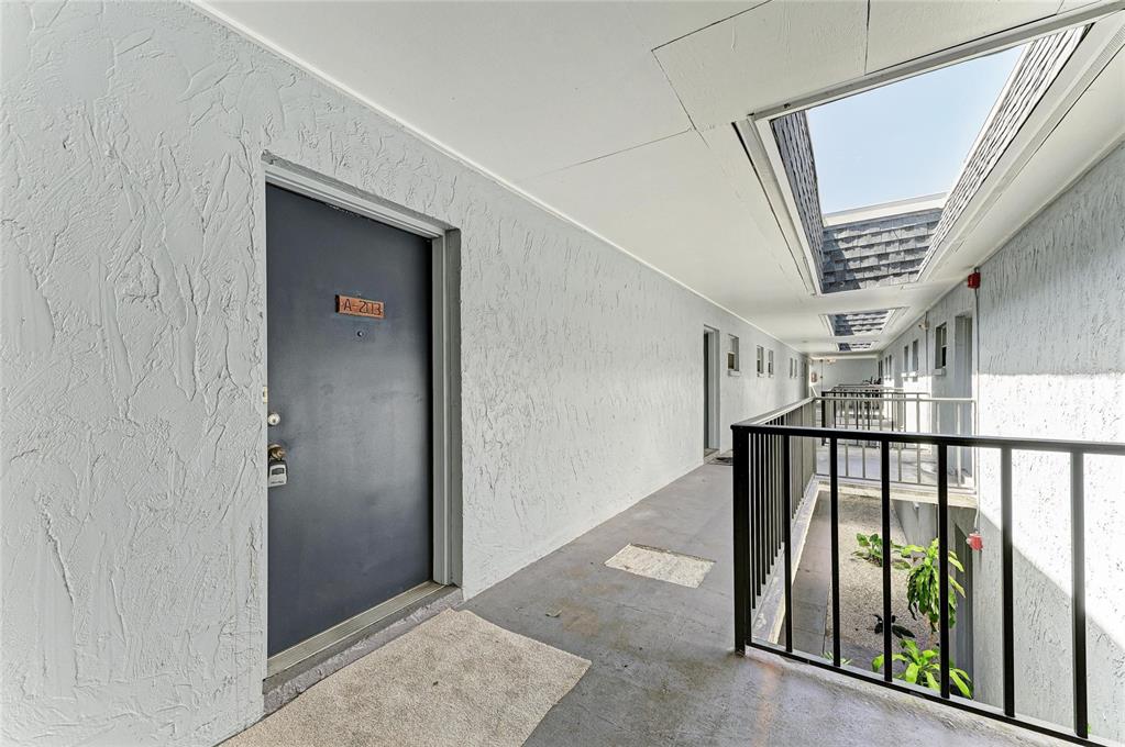 An outdoor apartment building walkway features a dark door labeled A-203 and black metal railings — 5503 FOUNTAIN LAKE CIRCLE UNIT A203, BRADENTON, FL