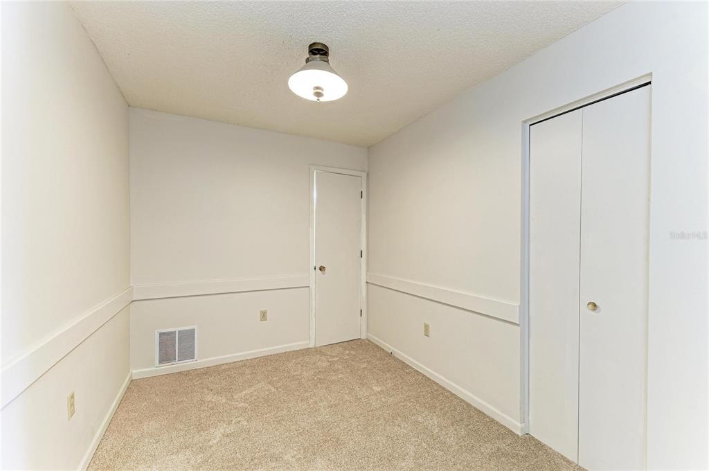 An empty bedroom with beige carpet, white walls, a ceiling light, and two closet doors — 5503 FOUNTAIN LAKE CIRCLE UNIT A203, BRADENTON, FL