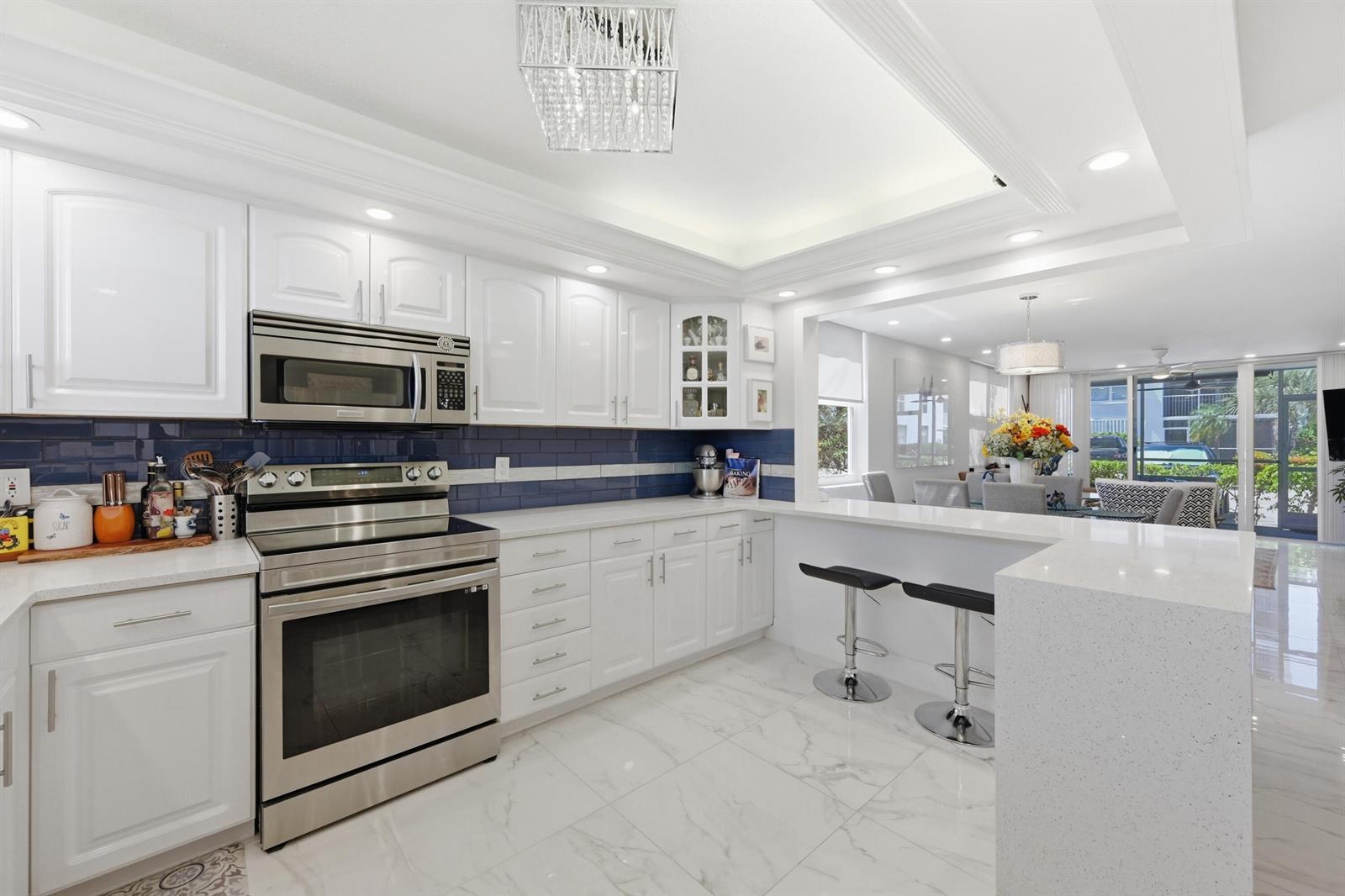 A modern kitchen features white cabinets, stainless steel appliances, blue subway tile, and quartz countertops — 2008 S Federal Highway # 101, Boynton Beach FL 33435, BOYNTON BEACH, FL