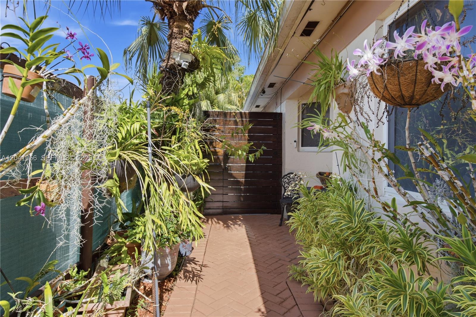A brick walkway leads to a wooden gate in a lush, plant-filled outdoor patio area — 9622 SW 146th Ave, Miami FL 33186, MIAMI, FL