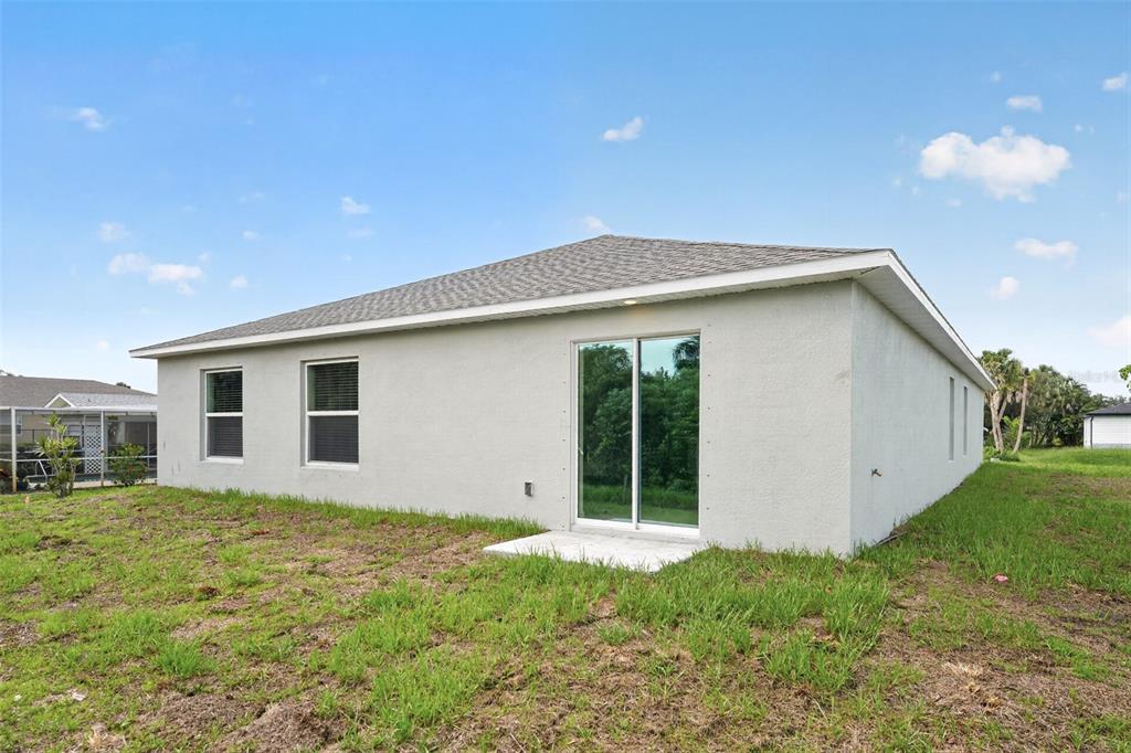 The rear exterior of a single-story house features a sliding glass door and two windows — 22568 ALCORN AVENUE, PORT CHARLOTTE, FL