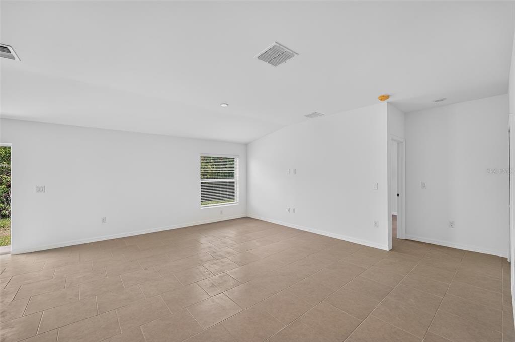 An empty room with white walls, tile flooring, and a window overlooking greenery — 22568 ALCORN AVENUE, PORT CHARLOTTE, FL
